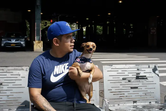a guy holds a chihuahua near an elevated subway track